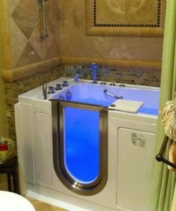 Walk in bathtub with blue LED light clear door and chrome fixtures in a tiled bathroom