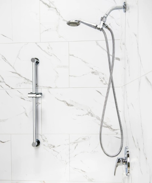 Chrome handheld shower on hose with vertical grab bar against white marble tile wall