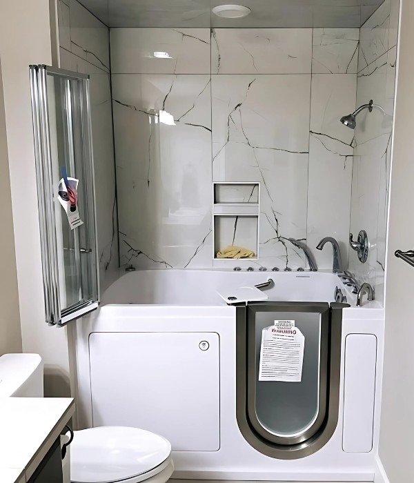 Walk in bathtub with frosted U door chrome fixtures and marble tile walls with shower niche