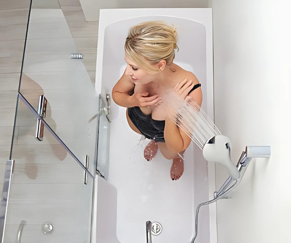 Top view of woman showering in a bathtub using a handheld shower head beside a glass panel